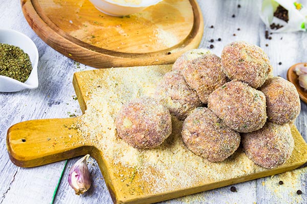 Albóndigas sin procesar en un tazón con los ingredientes en el fondo de madera